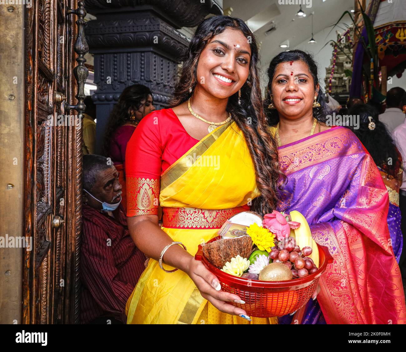 Lewisham, London, UK, 11th Sep 2022. Two ladies ladies smile on their way into the temple, carrying fruit as Prasada, an offering to the deities. Worshippers arrive in a steady stream to the beautifully decorated temple. Worshippers mark the Hindu Chariot Festival Ther Thiruvizha with a colourful celebration. Out of respect for the Queen, the procession is today restricted to just the Sivan Kovil temple and courtyard. Normally, around 5,000 visitors and participants would proceed from the temple through the town centre carrying large chariots and offerings. Stock Photo