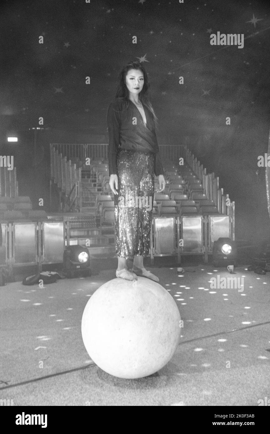 Girl standing on a globe wearing sequin trousers and black top in a circus ring Stock Photo