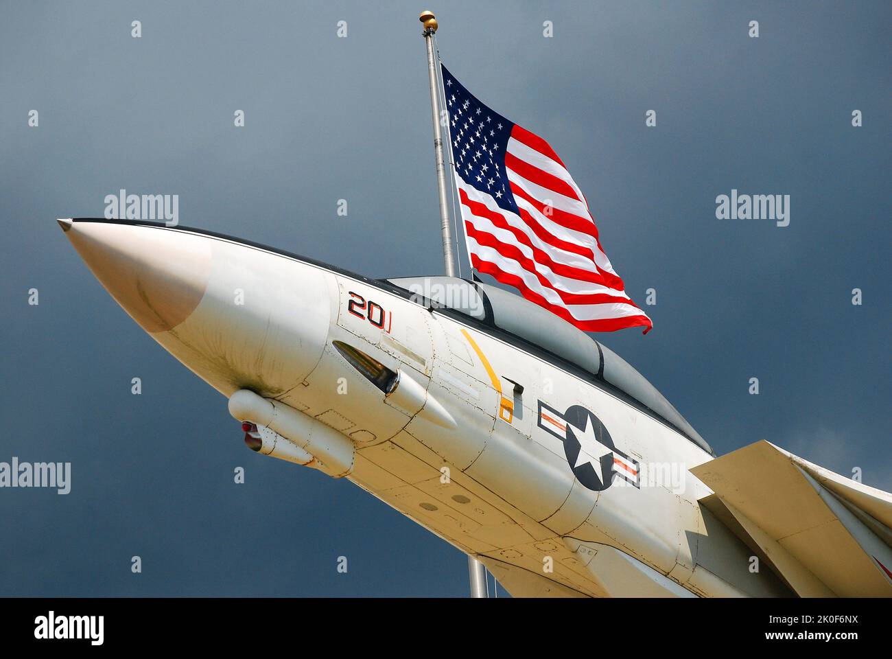 An American Grumman F14 Tom Cat appears to fly with an American flag at the entrance to the  National Museum of Naval Aviation in Pensacola, Florida Stock Photo