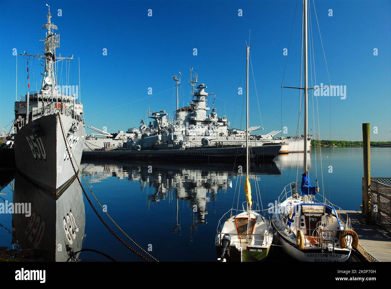 The Battleship USS Massachusetts and destroyer USS Joseph P Kennedy are reflected int he still water of Fall River Stock Photo