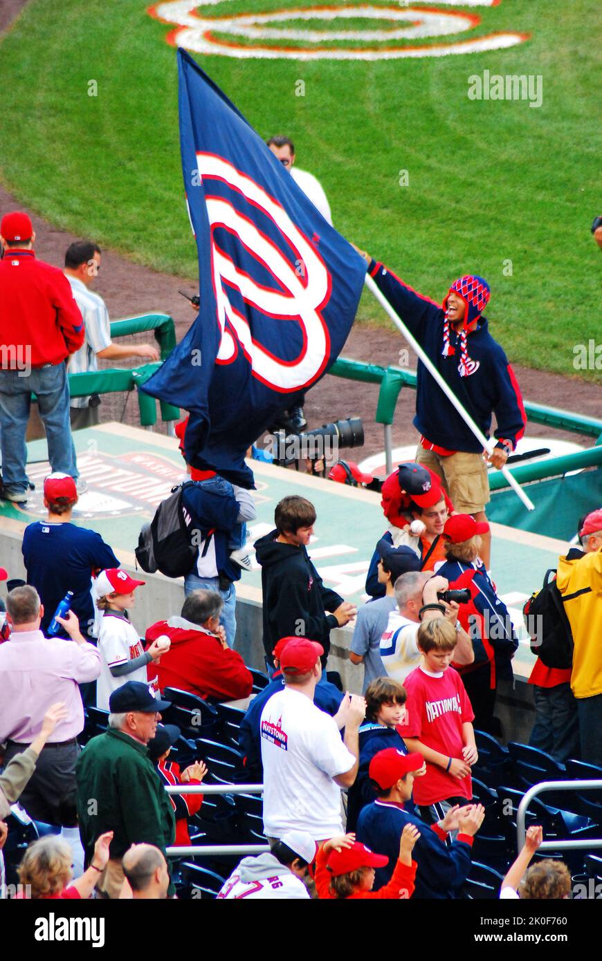 A man stands on top of the dugout at Washington Nationals ballpark, waving the baseball team's flag to lead the crowd in cheering for the club Stock Photo
