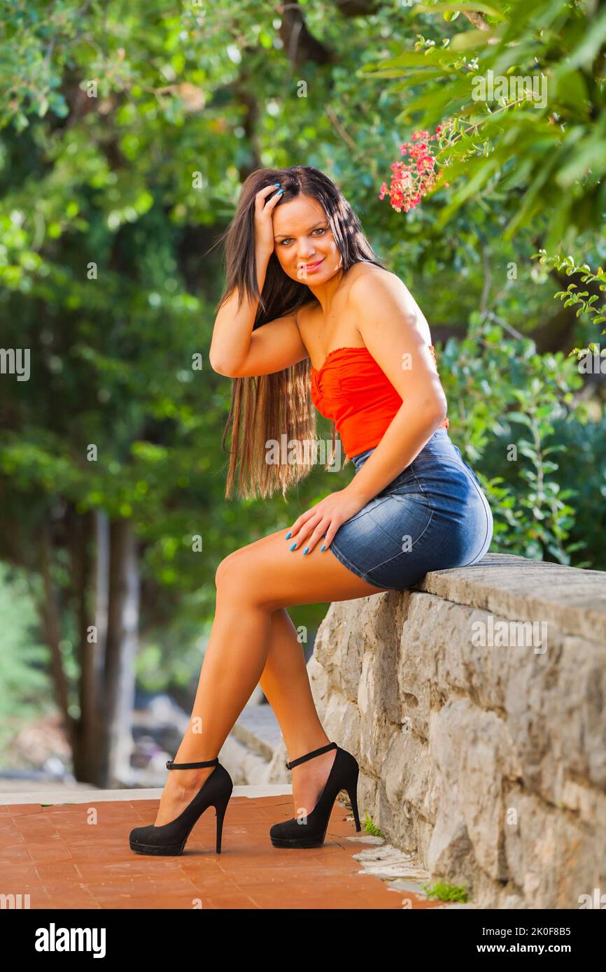 Teen girl denim miniskirt legs heels looking at camera seducing hand touching touch hair posing smiling Stock Photo