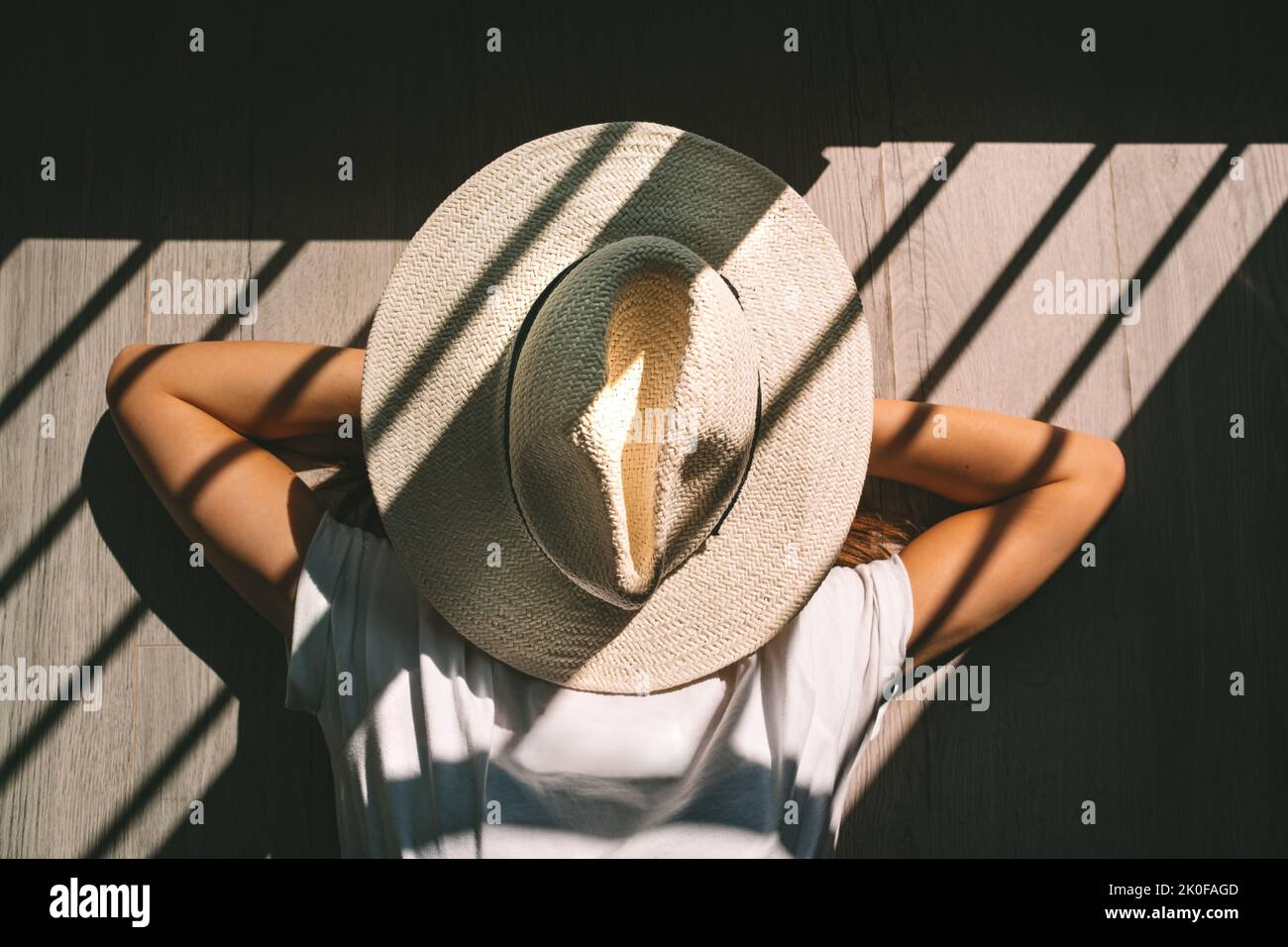 Young woman with hat on head laying on the ground on sunset. Woman enjoying free time and lazy weekend. Stock Photo