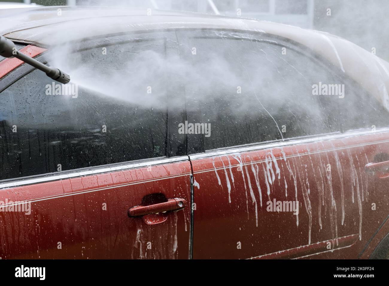 He washes his car under high pressure jet sprays with water while he cleans the car with a brush