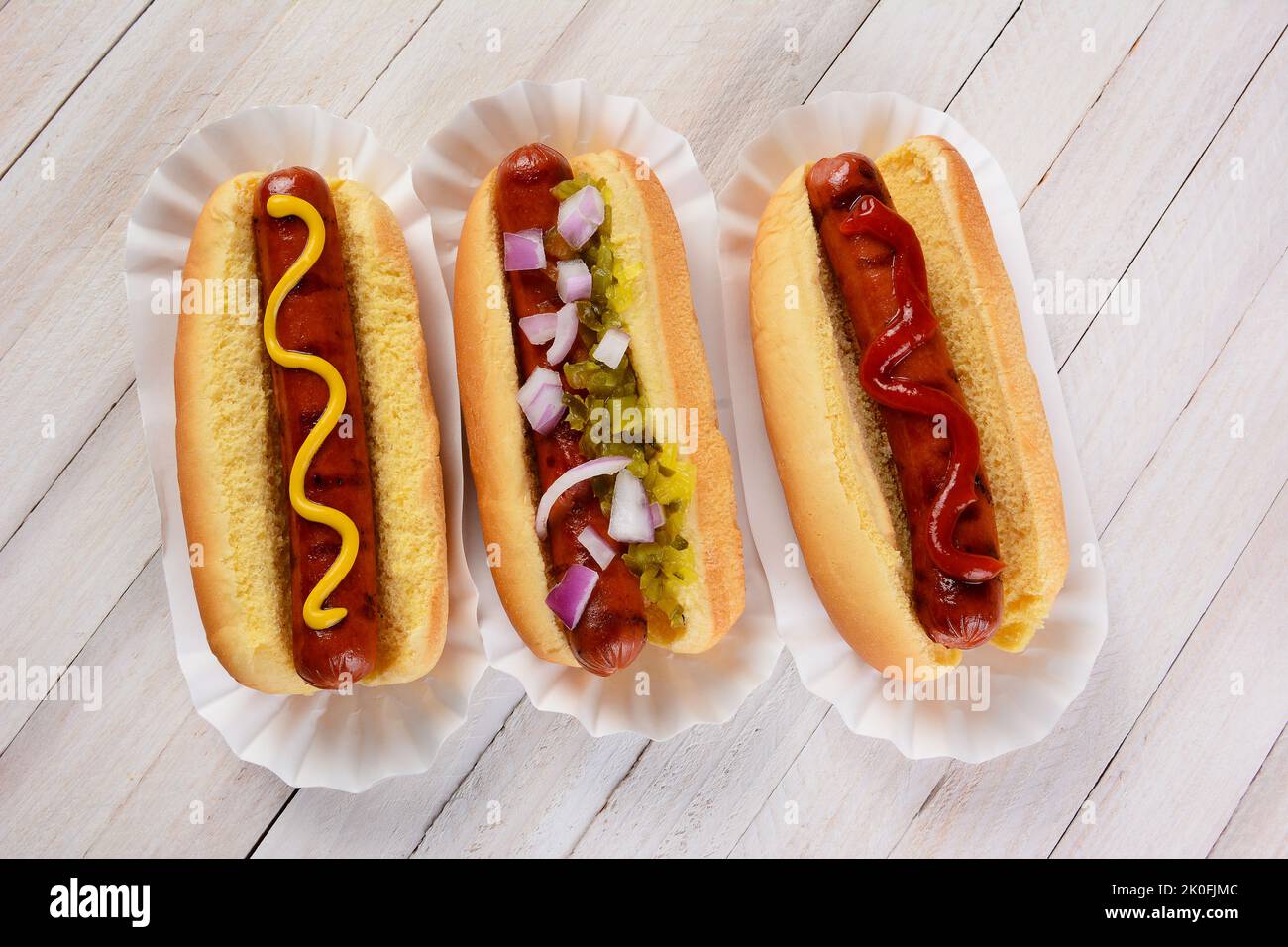 Top view of three hot dogs on a wood table with different condiments