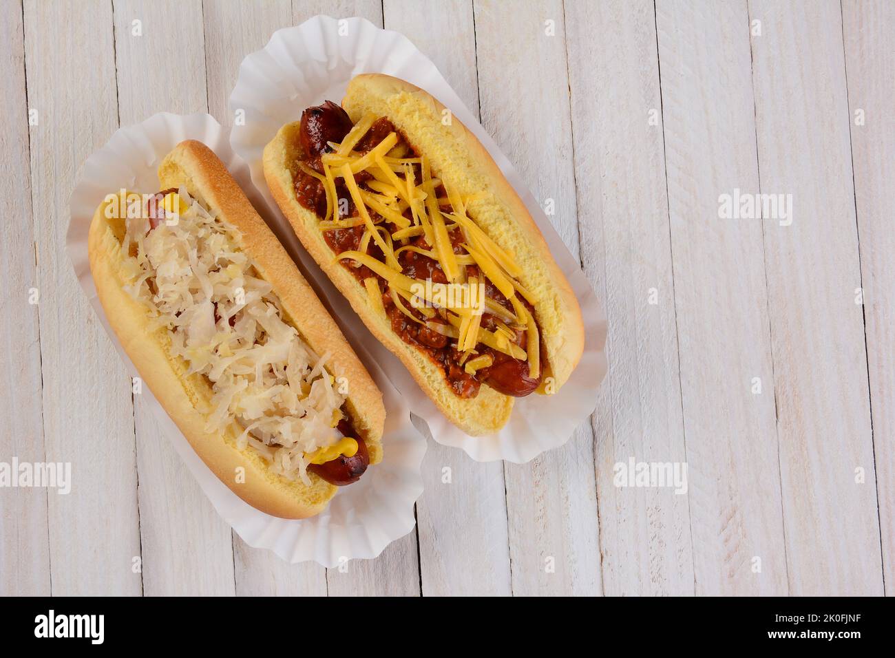 Two hot dogs one with sauerkraut and another with chili cheese toppings on a white ewood table with copy space. Stock Photo