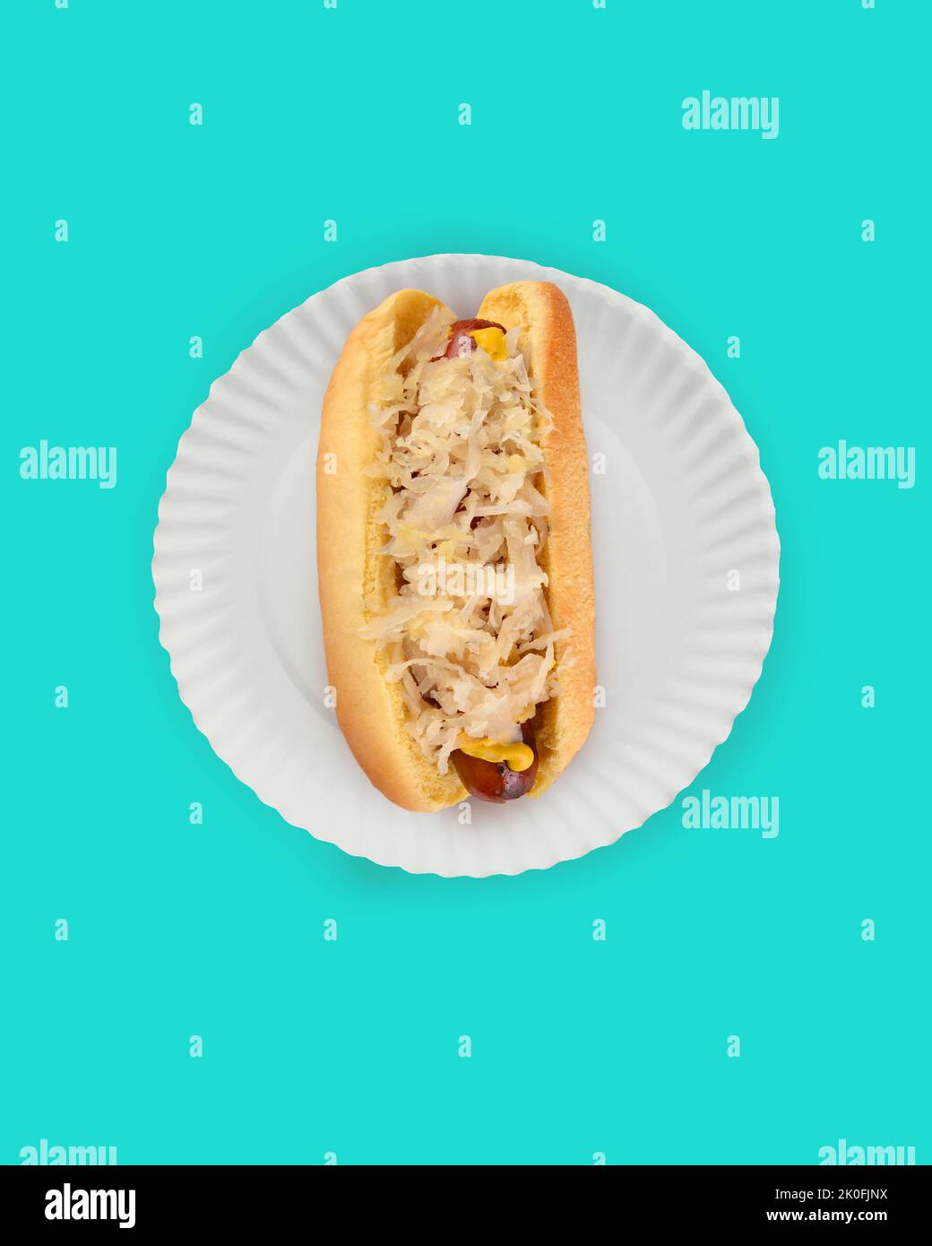 Flat Lay Hot Dog in Bun Still Life. Fankfurter in bun with Sauerkraut on a white paper plate on teal background with copy space. Stock Photo