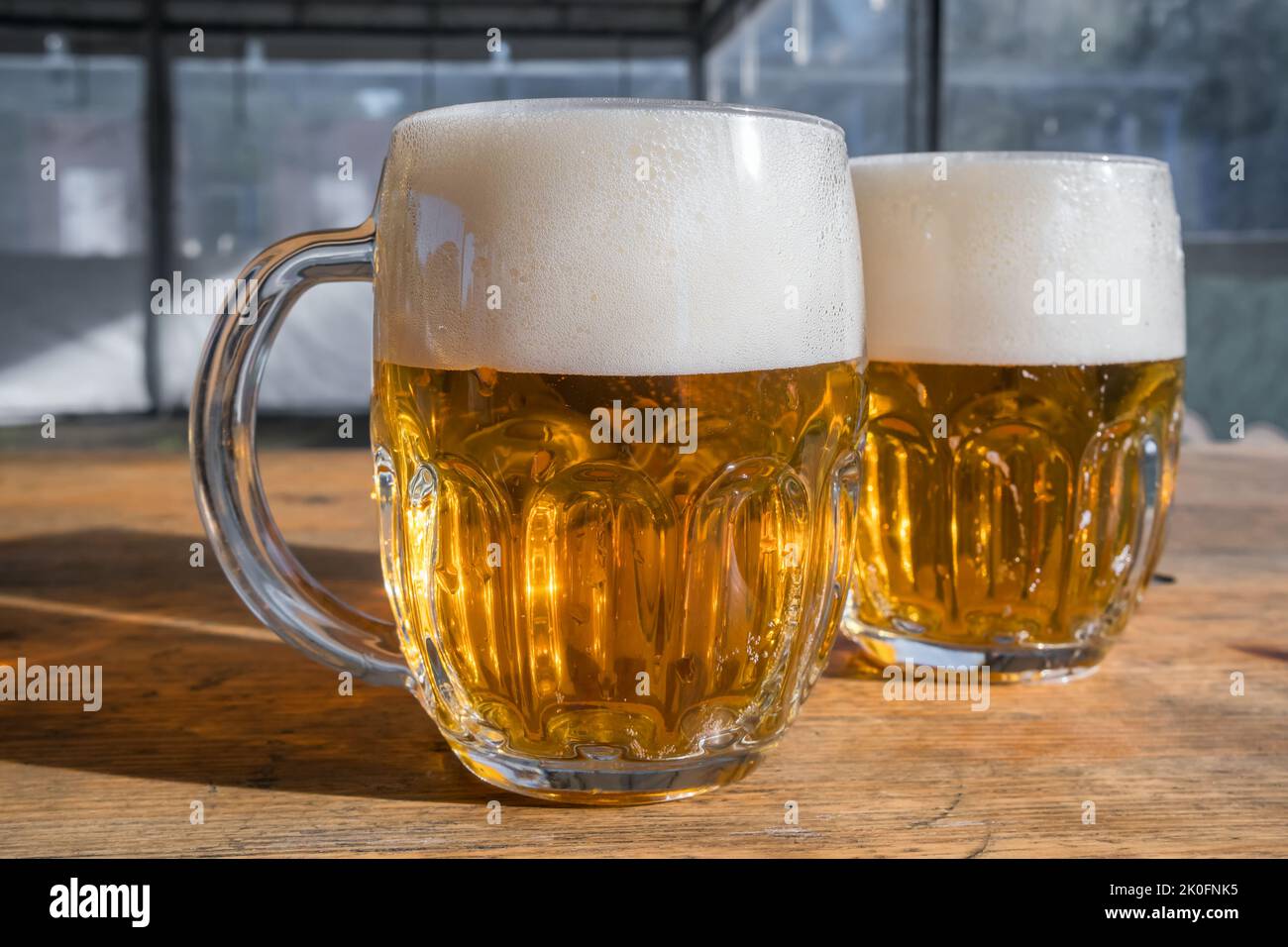 Two mugs of light beer with foam on a wooden table Stock Photo