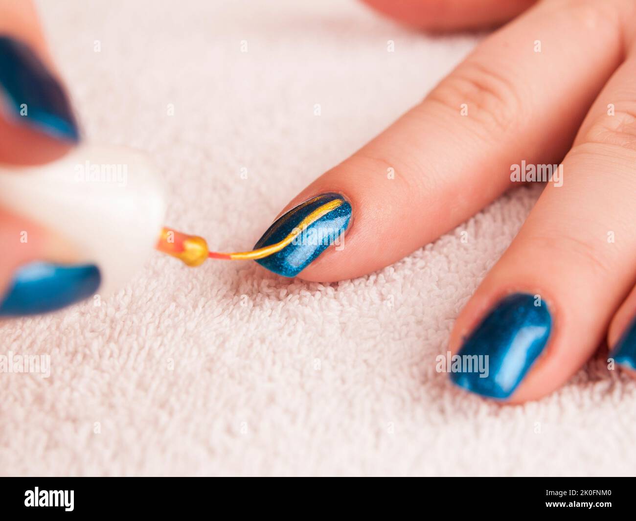 Painting modern nail art with gold nail polish on blue base Stock Photo