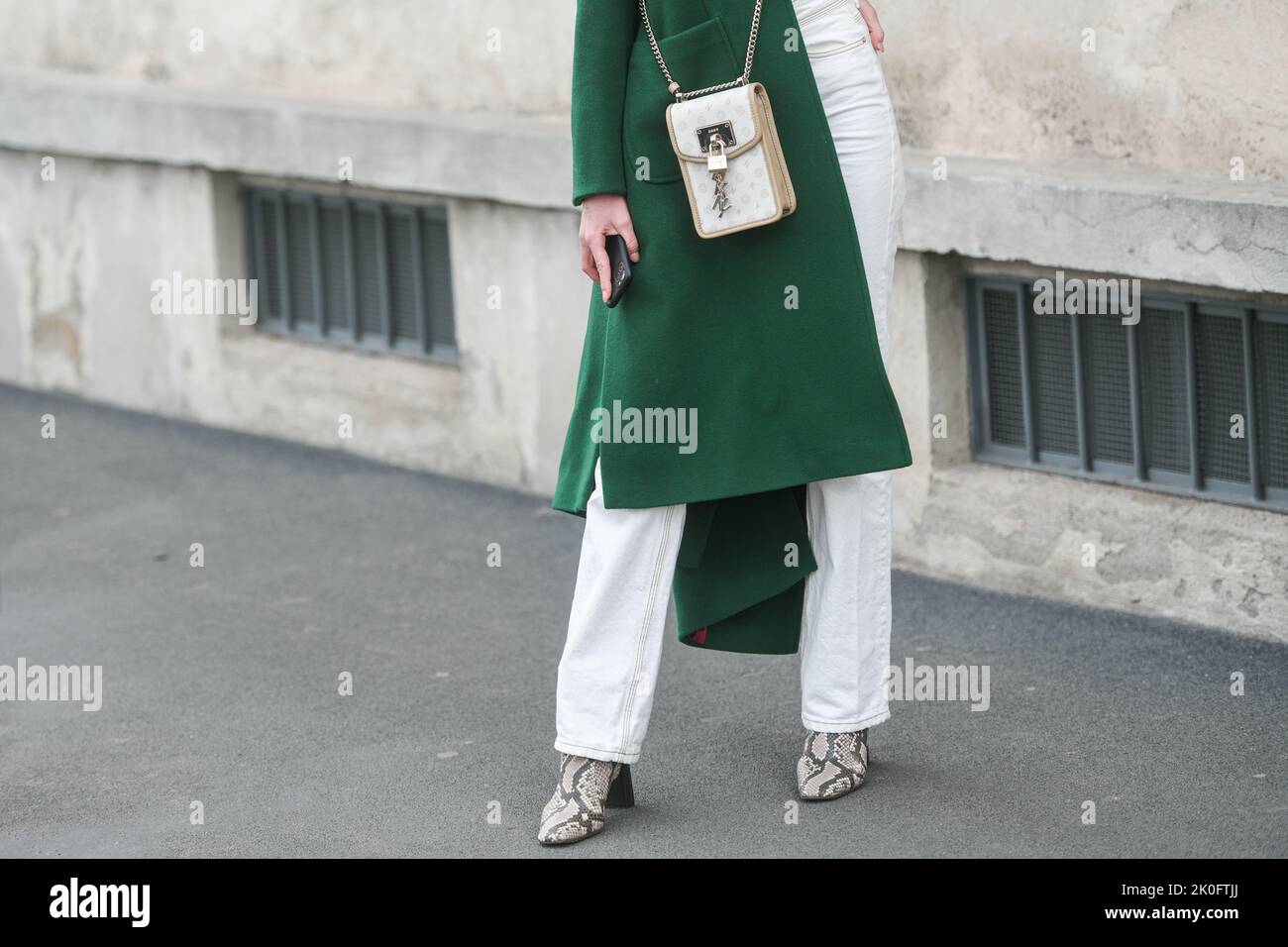 Milan, Italy - February, 24: Street style, woman wearing a dark green coat, a white handbag, white pants, snake print pattern ankle boots. Stock Photo