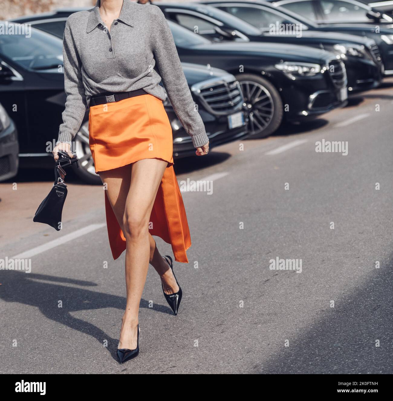 Milan, Italy - February, 24: Street style, woman wearing a Prada outfit: orange skirt, grey zipper, black bag, sunglasses, heels. Stock Photo