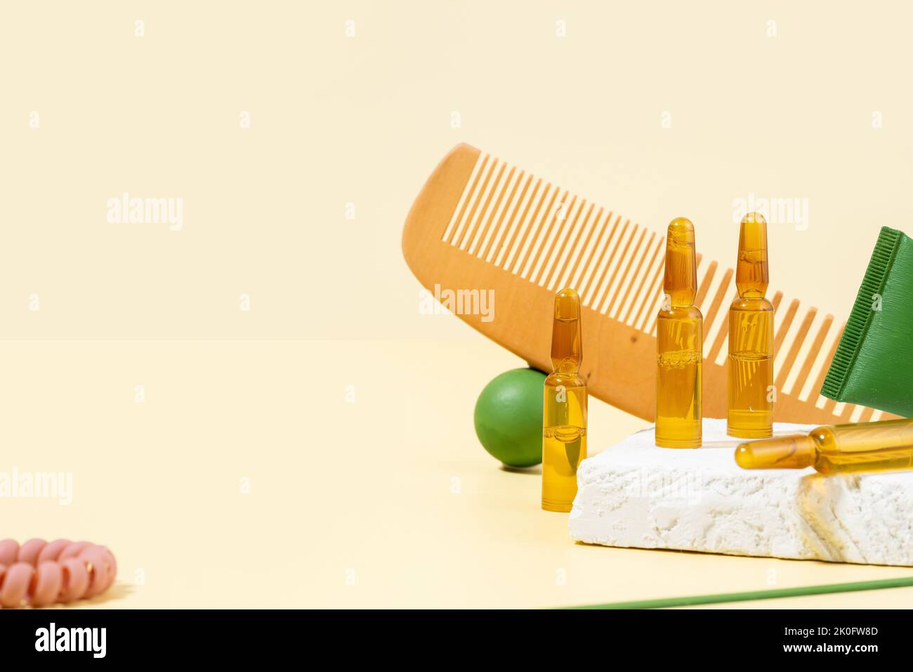 Cosmetic ampoules with serum for hair growth, restoration. Hair comb and green props on a beige