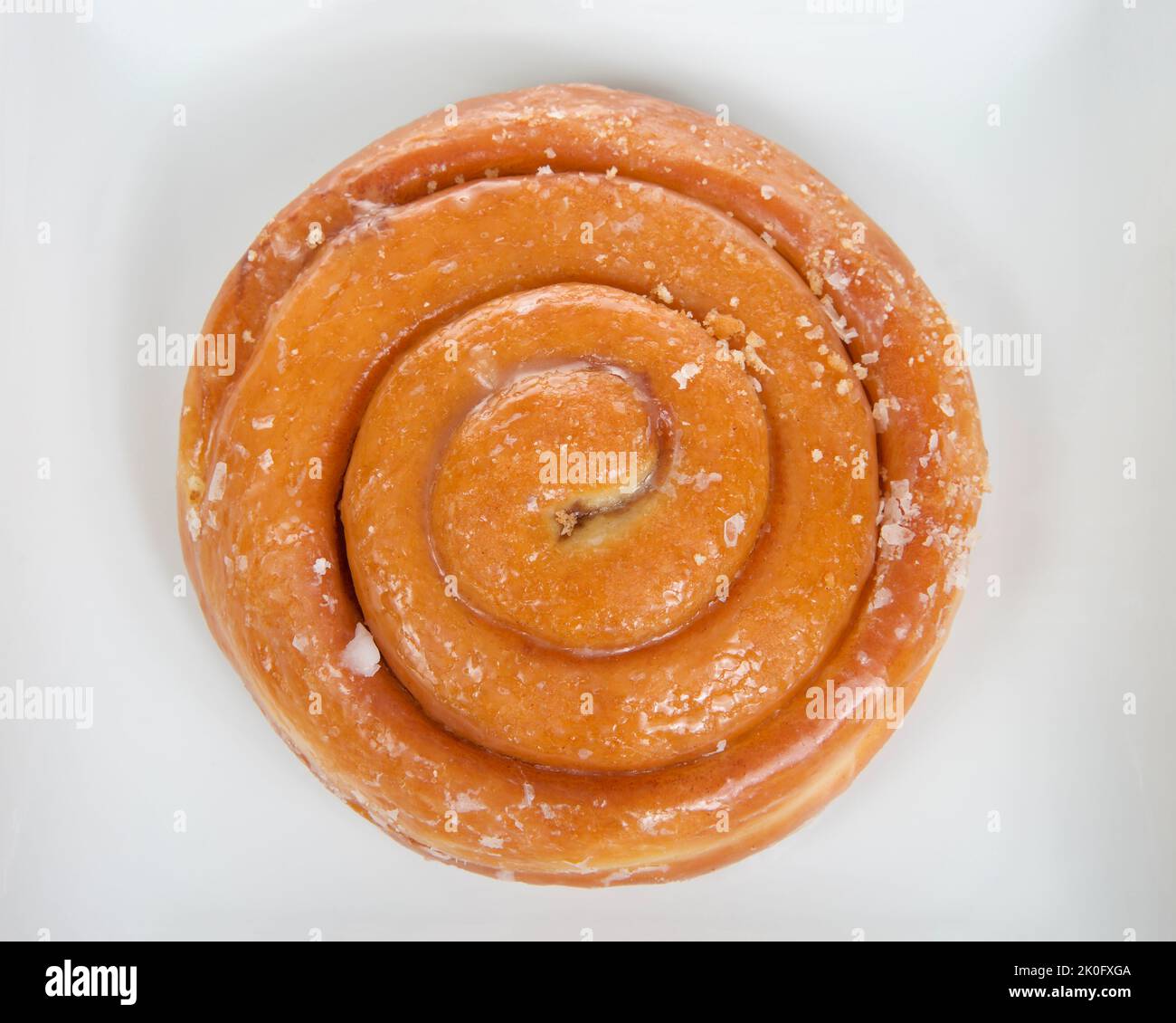 Top view flat lay of one cinnamon roll large round donut on a square off white porcelain plate, isolated on white Stock Photo