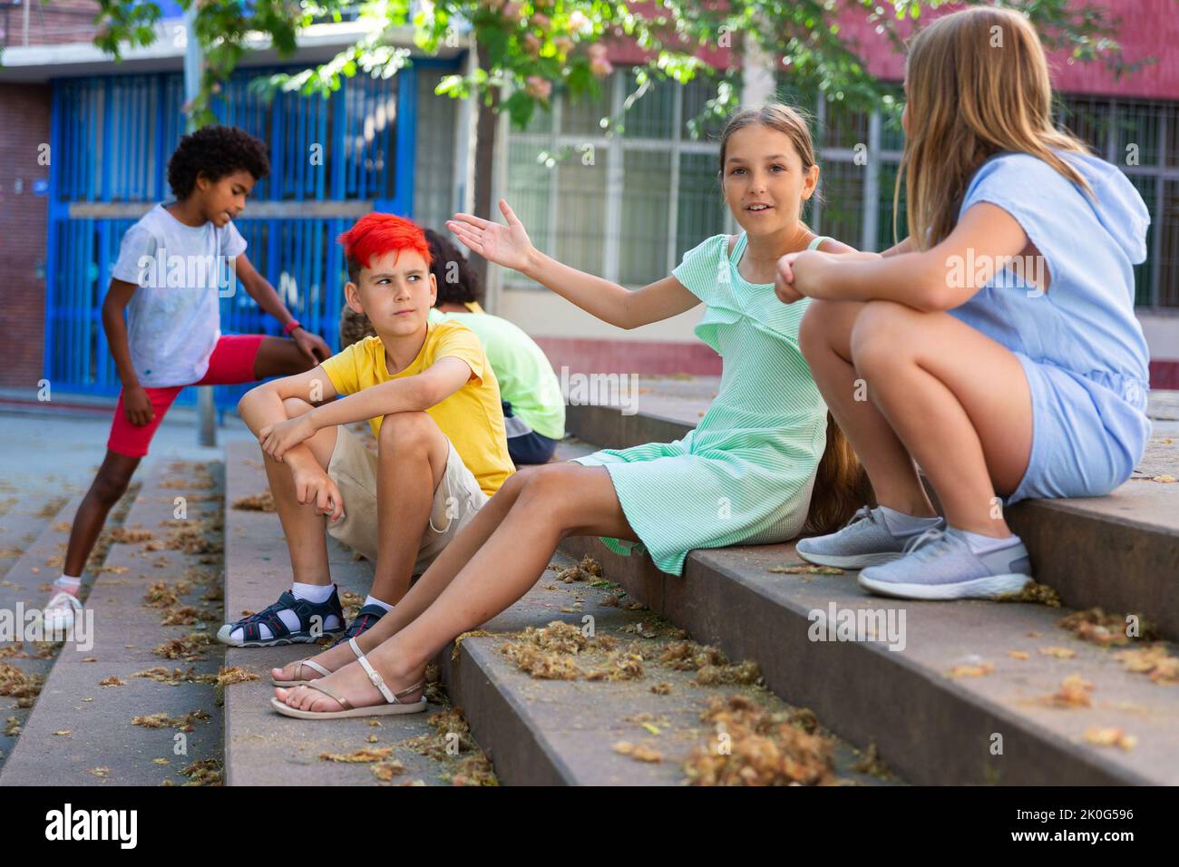 Positive tweenagers friendly blabbing while sitting on steps outdoors Stock Photo