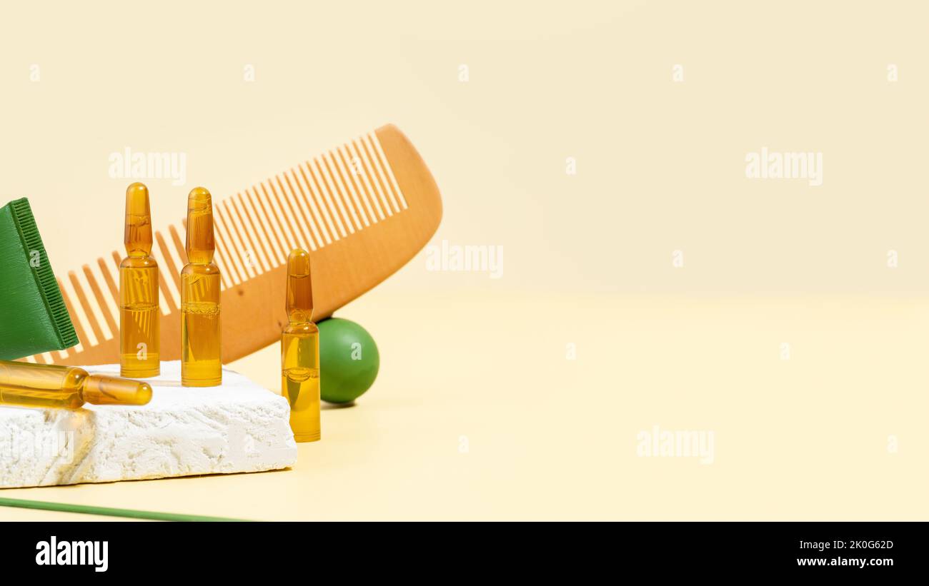Cosmetic ampoules with serum for hair growth, restoration. Hair comb and green props on a beige