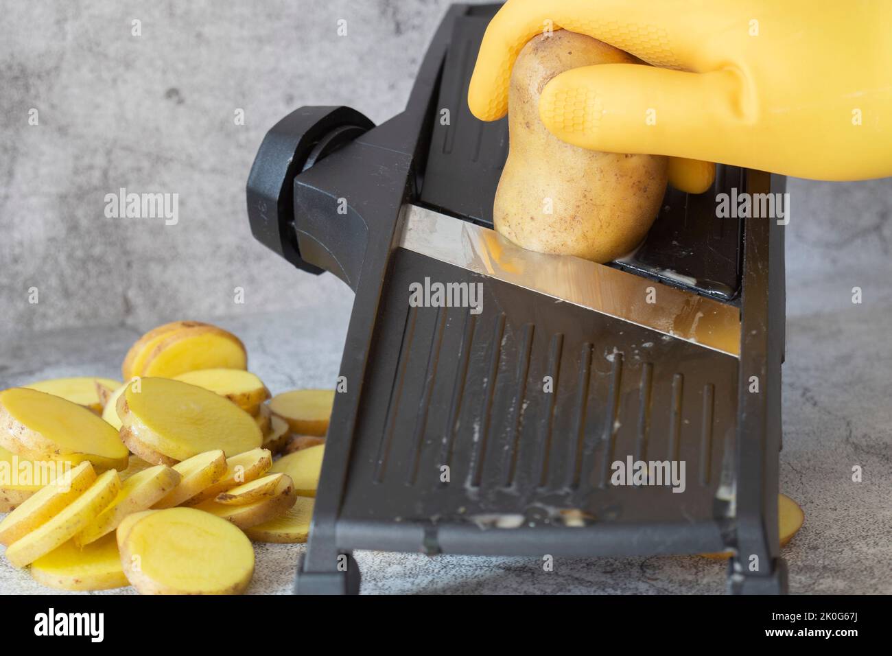https://c8.alamy.com/comp/2K0G67J/person-slicing-potato-on-a-kitchen-mandolin-cutter-on-a-concrete-background-2K0G67J.jpg