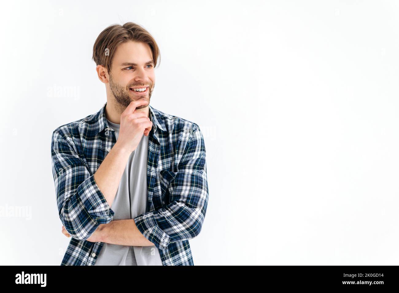 Photo of an attractive confident caucasian stylish young man, in casual clothes, standing on a white isolated background, looking to the side, thinking, smiling friendly. Space for presentation Stock Photo