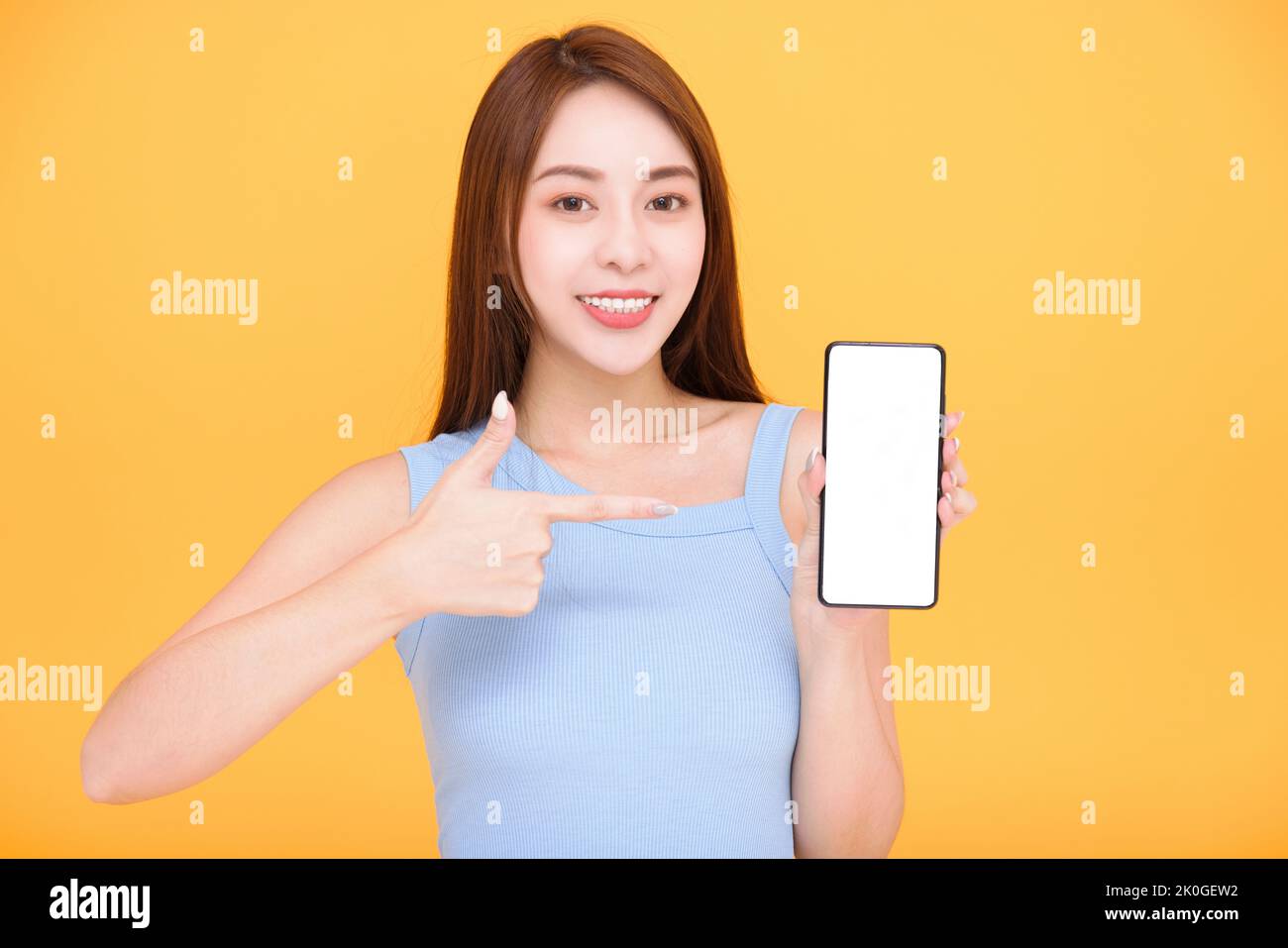 Happy asian woman showing mobile phone blank screen on yellow background Stock Photo