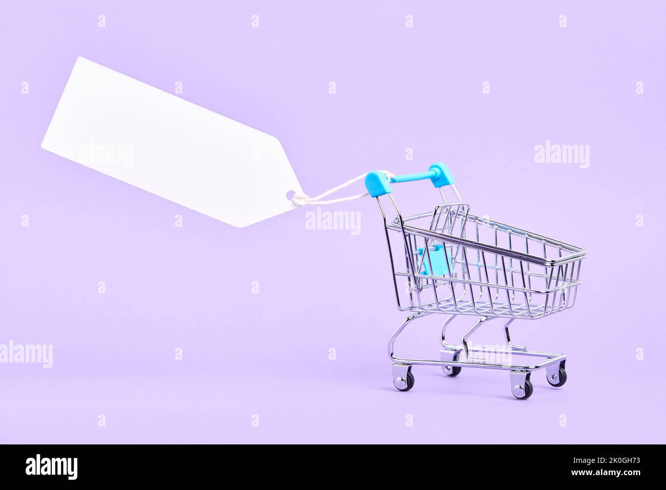 Empty shopping cart with a blank label on a pastel lilac background. Minimalist design with copy space. Concepts: market deals, seasonal sales and dis Stock Photo