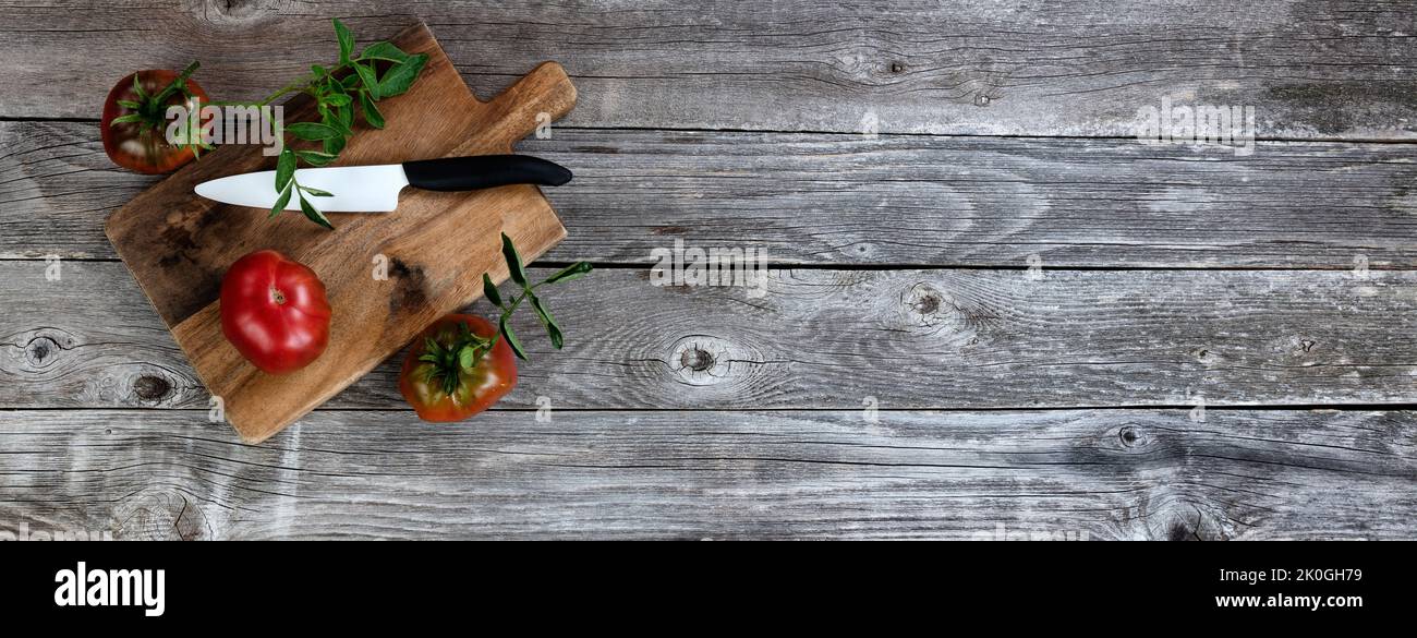 Ripe organic tomatoes with cutting knife plus server on rustic wood table in flat lay format Stock Photo