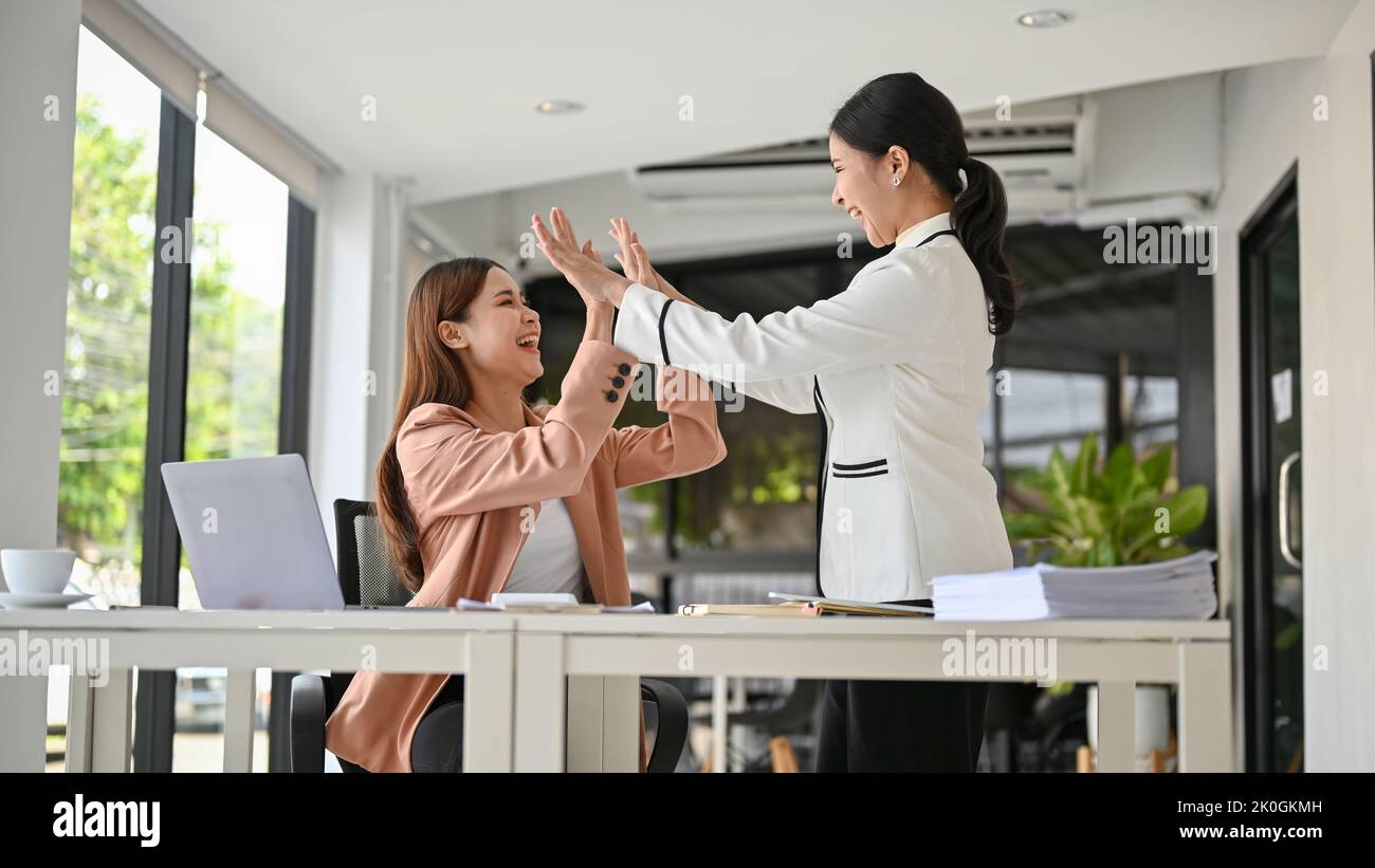 Two happy young Asian businesswomen celebrates their success together ...