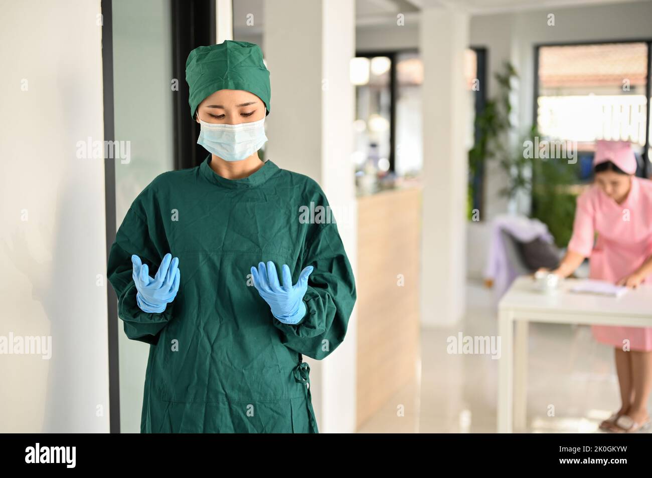 Professional and expert Asian female surgeon in green surgical gown and medical mask success with her surgery, standing in front of the Operating room Stock Photo