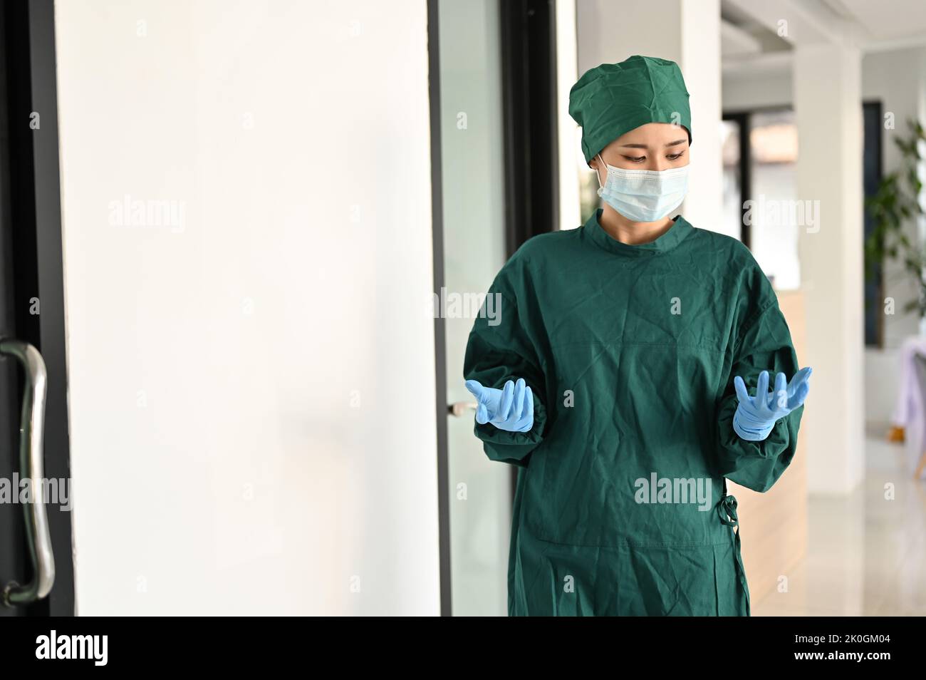 Professional Asian female doctor or surgeon in green surgical gown and medical mask walking along the operating room. Health care and surgery concept Stock Photo