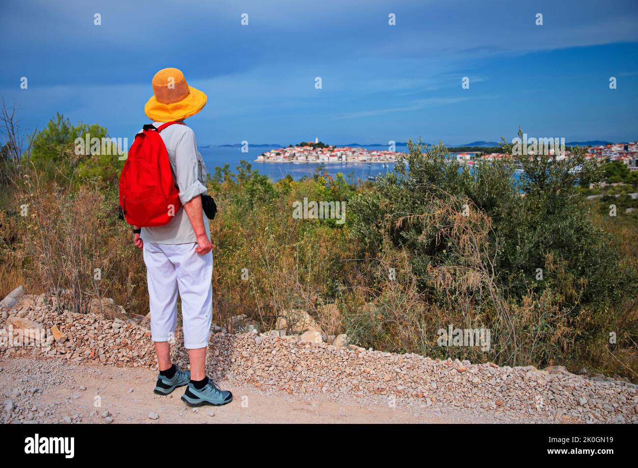 Senior woman standing on the hill looking at cityscape of Mediterranean town over the sea Stock Photo