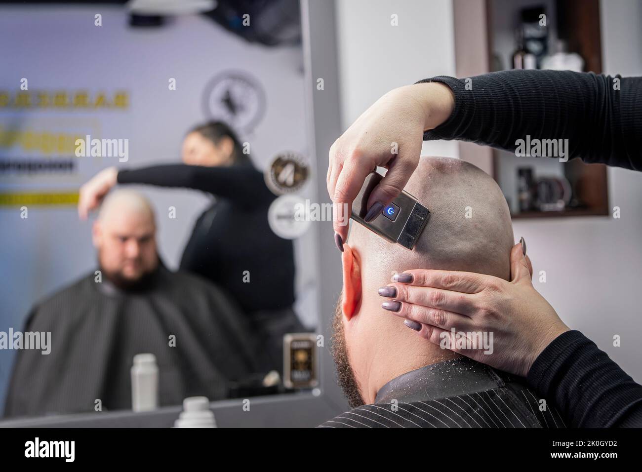 The hands of young barber making haircut to attractive man in barbershop. shave your bald head Stock Photo