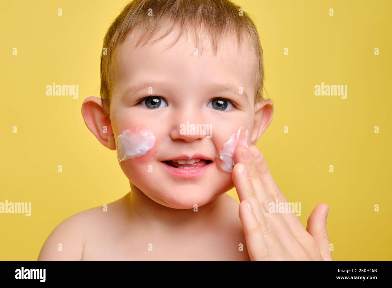 Mother smears allergy cream on face of toddler baby, studio yellow