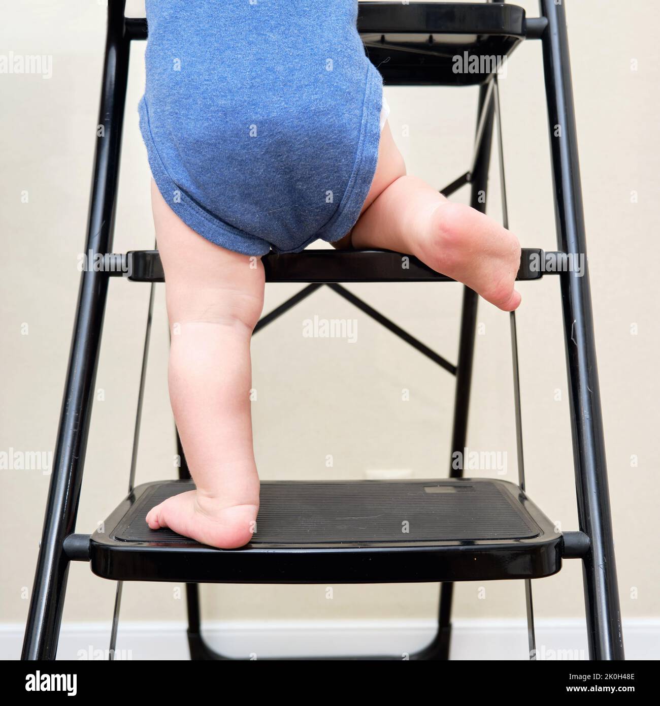 Toddler baby climbs on the steps ladder. Child boy climbs up the stairs