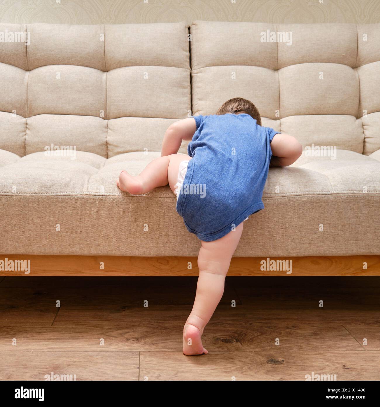 Toddler baby climbs on the sofa. Child boy learning to get off the bed