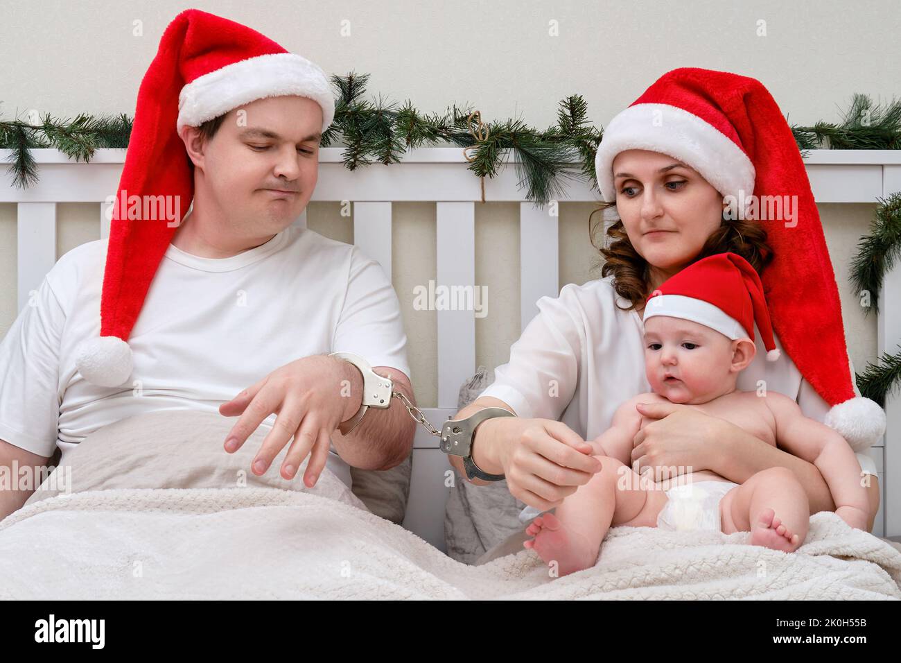 Man and woman with child handcuffed on bed decorated for christmas and Handcuffed For Christmas