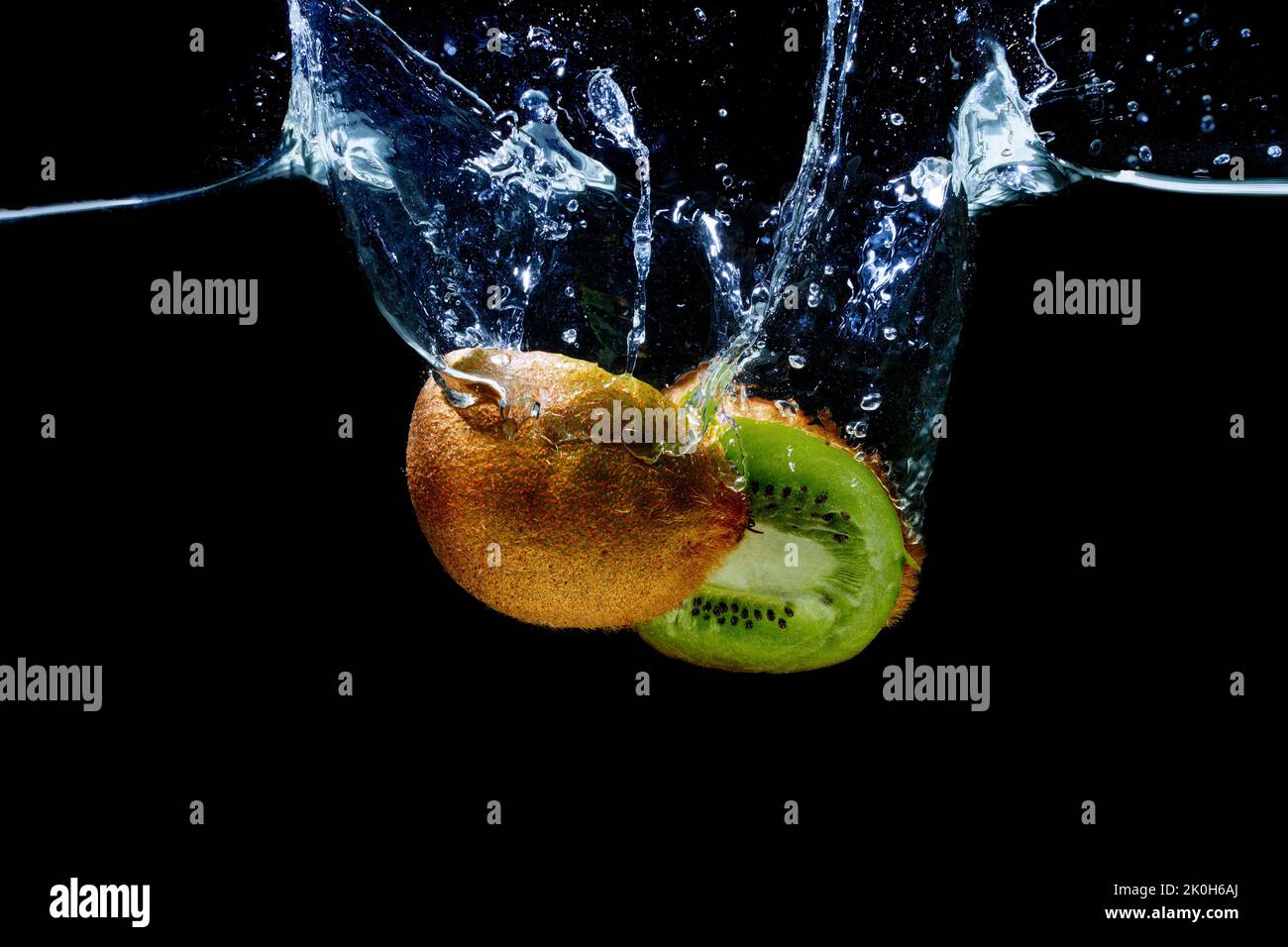 Cut-in-half kiwifruit dropped in water with splashes isolated on black background Stock Photo