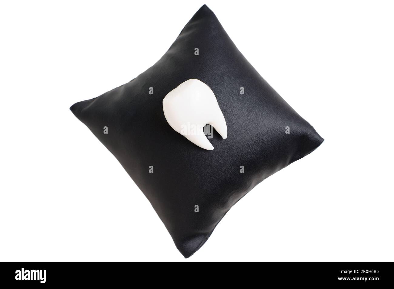 Large white tooth on a black leather pillow isolated on white. Comfortable dental care concept. Stock Photo