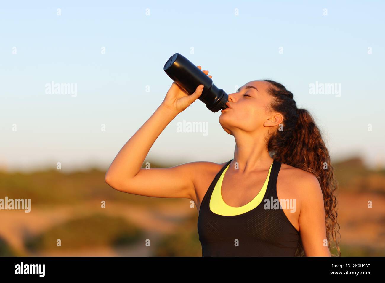 Runner drinking from bottle standing at sunset Stock Photo
