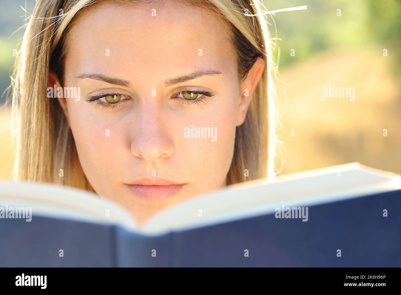Front view close up portrait of a young woman reading a paper book in nature Stock Photo