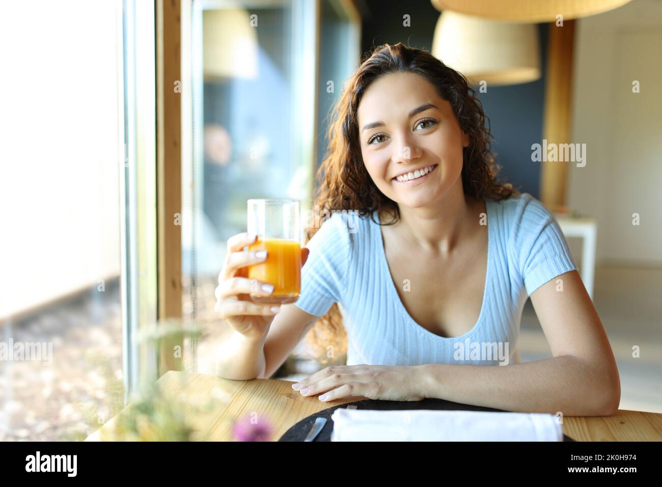 Woman holding orange juice glass looking at camera in a restaurant Stock Photo
