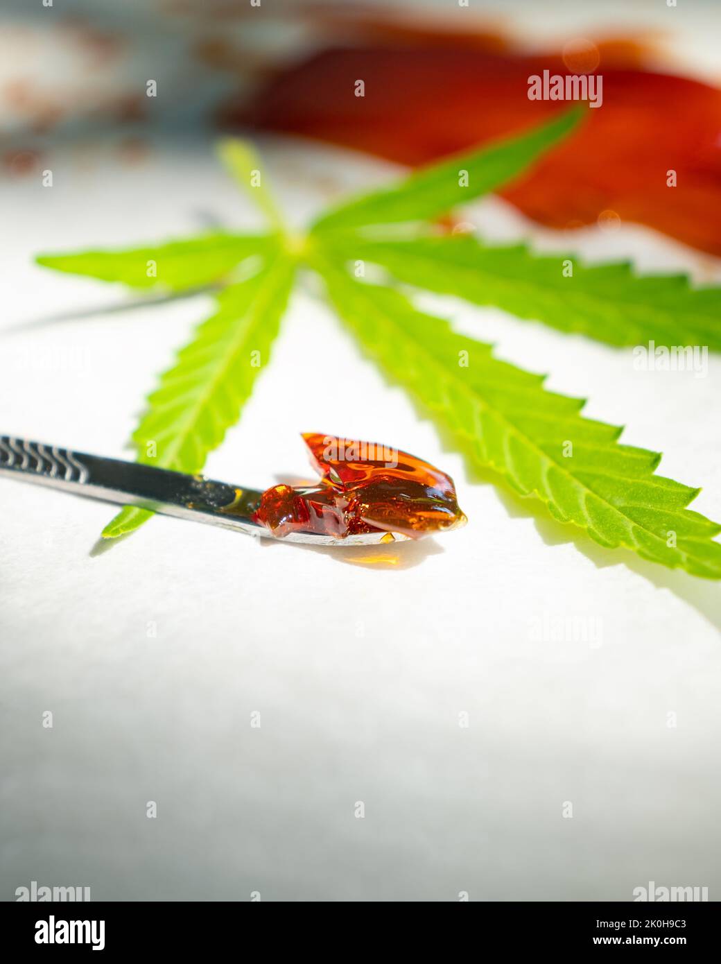 a piece of cannabis wax on a stick and a green leaf, high thc resin. Stock Photo