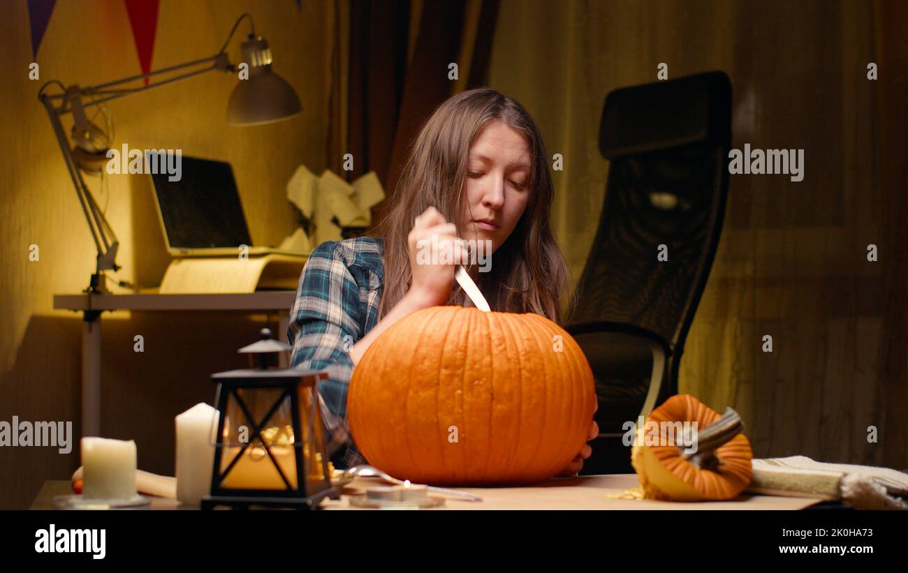 Preparing pumpkin for Halloween. Woman sitting and carving with knife halloween Jack O Lantern pumpkin at home for her family. Stock Photo