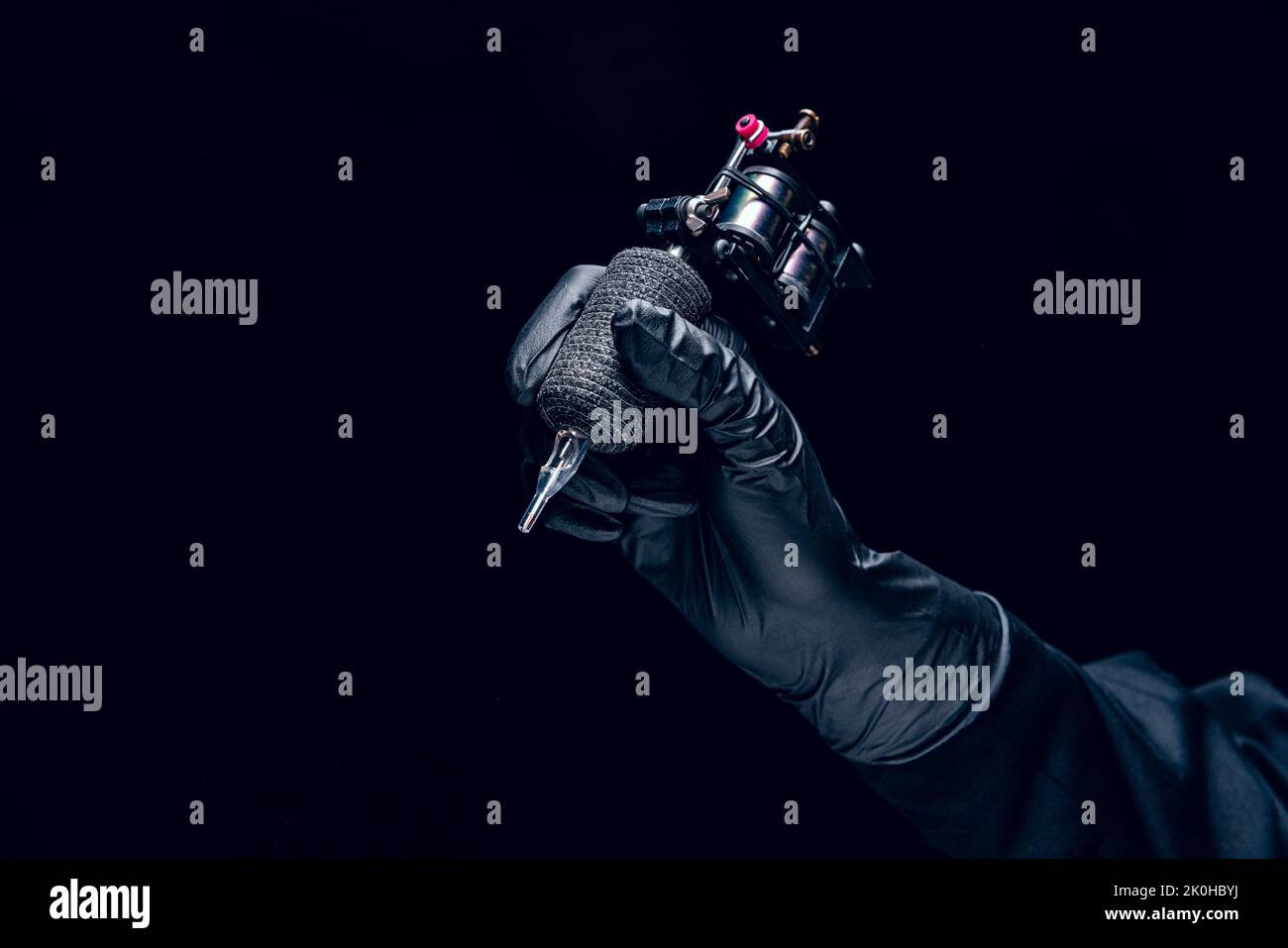 Machine for tattoo. Human hand in black protective glove holding professional equipment for making tattoo on body isolated on dark background. Stock Photo