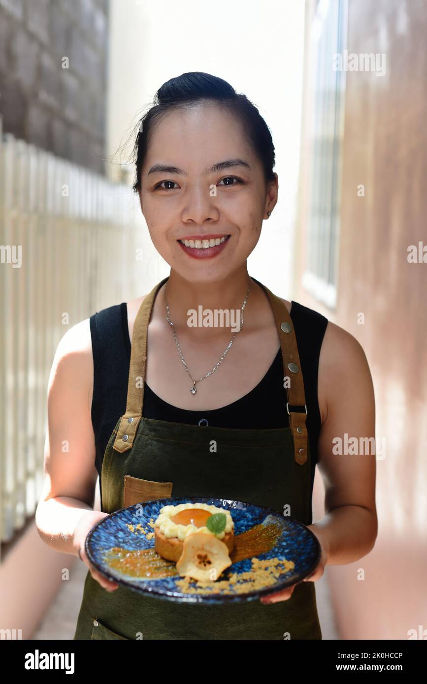 Vietnamese woman waitress in apron holding apple tart on a blue plate Stock Photo