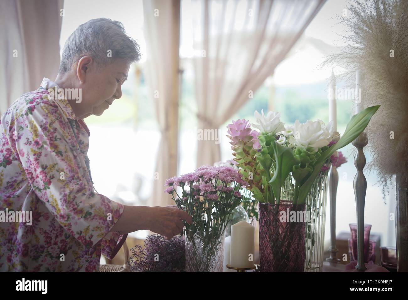 old woman decorate flower bouquet in glass vase on dining table Stock Photo