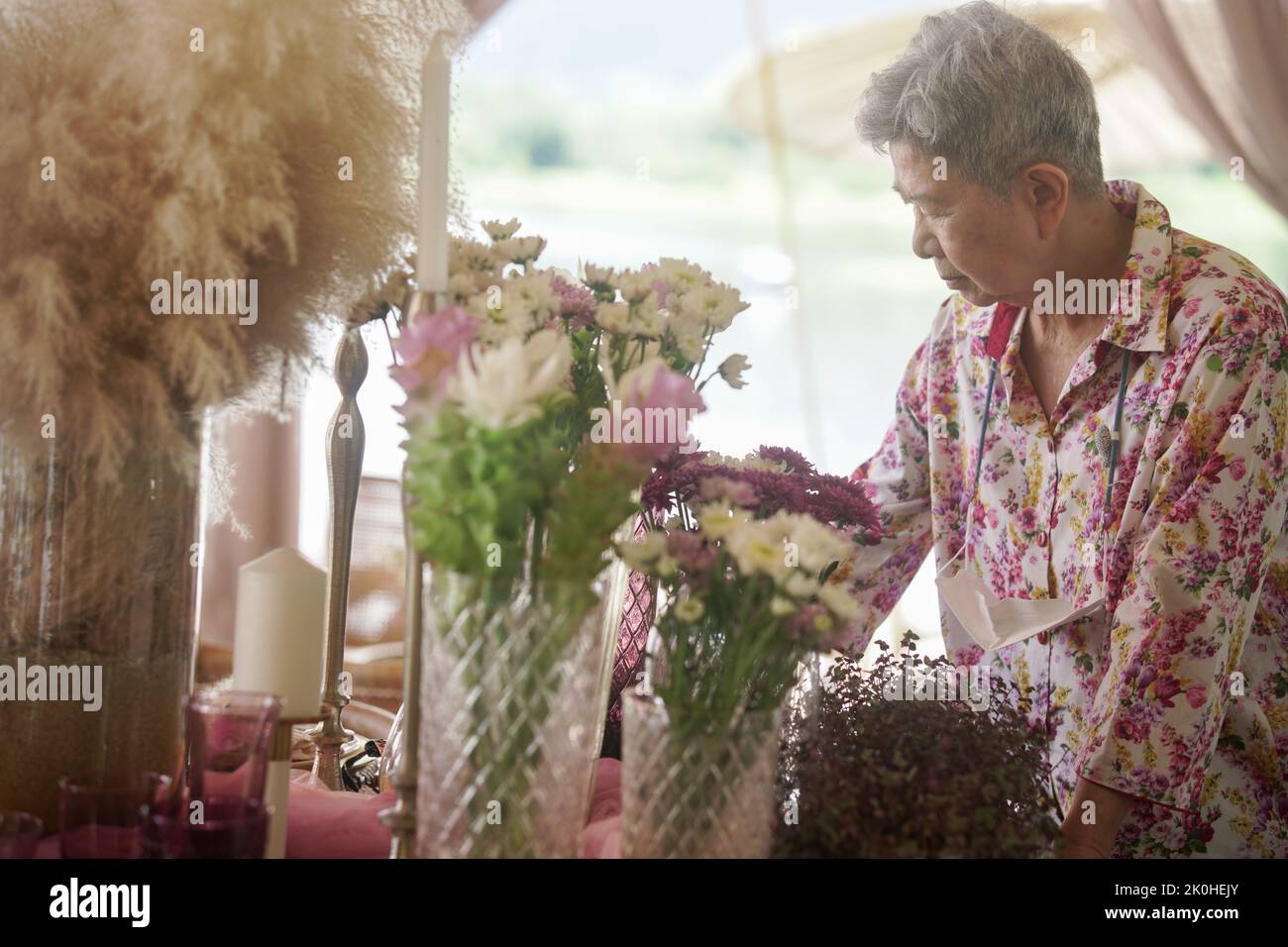 old woman decorate flower bouquet in glass vase on dining table Stock Photo