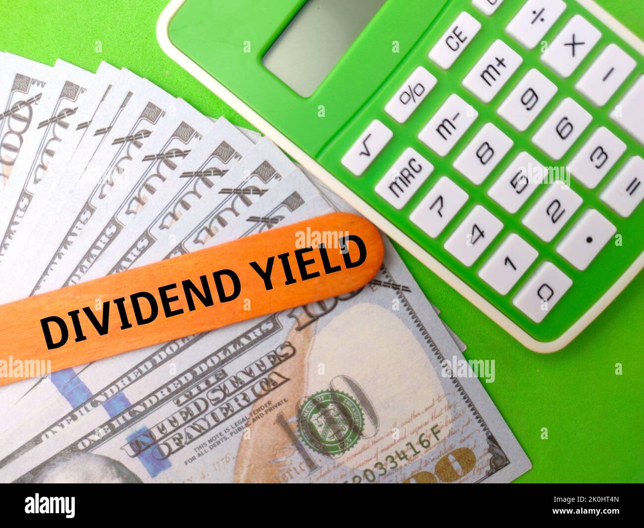 A flat flay with a Calculator and banknotes with the word DIVIDEND YIELD on a green background Stock Photo