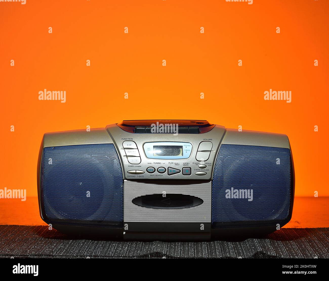A vintage CD and cassette boombox on a table against an orange