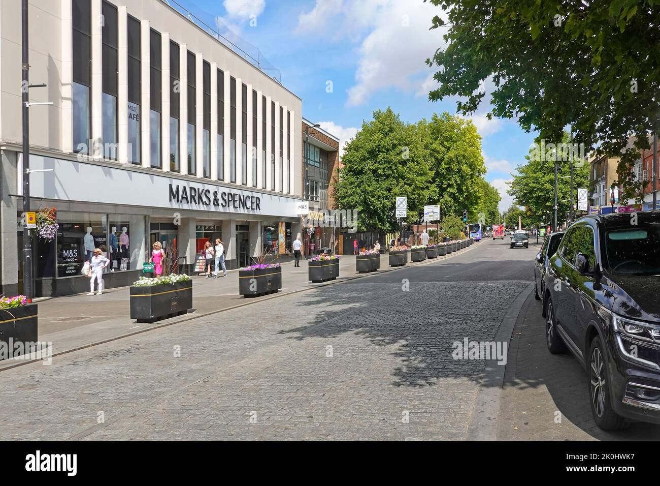 Brentwood cobbled shopping High Street with Marks & Spencer store cafe building façade summer planter boxes & on road car parking Essex England UK Stock Photo