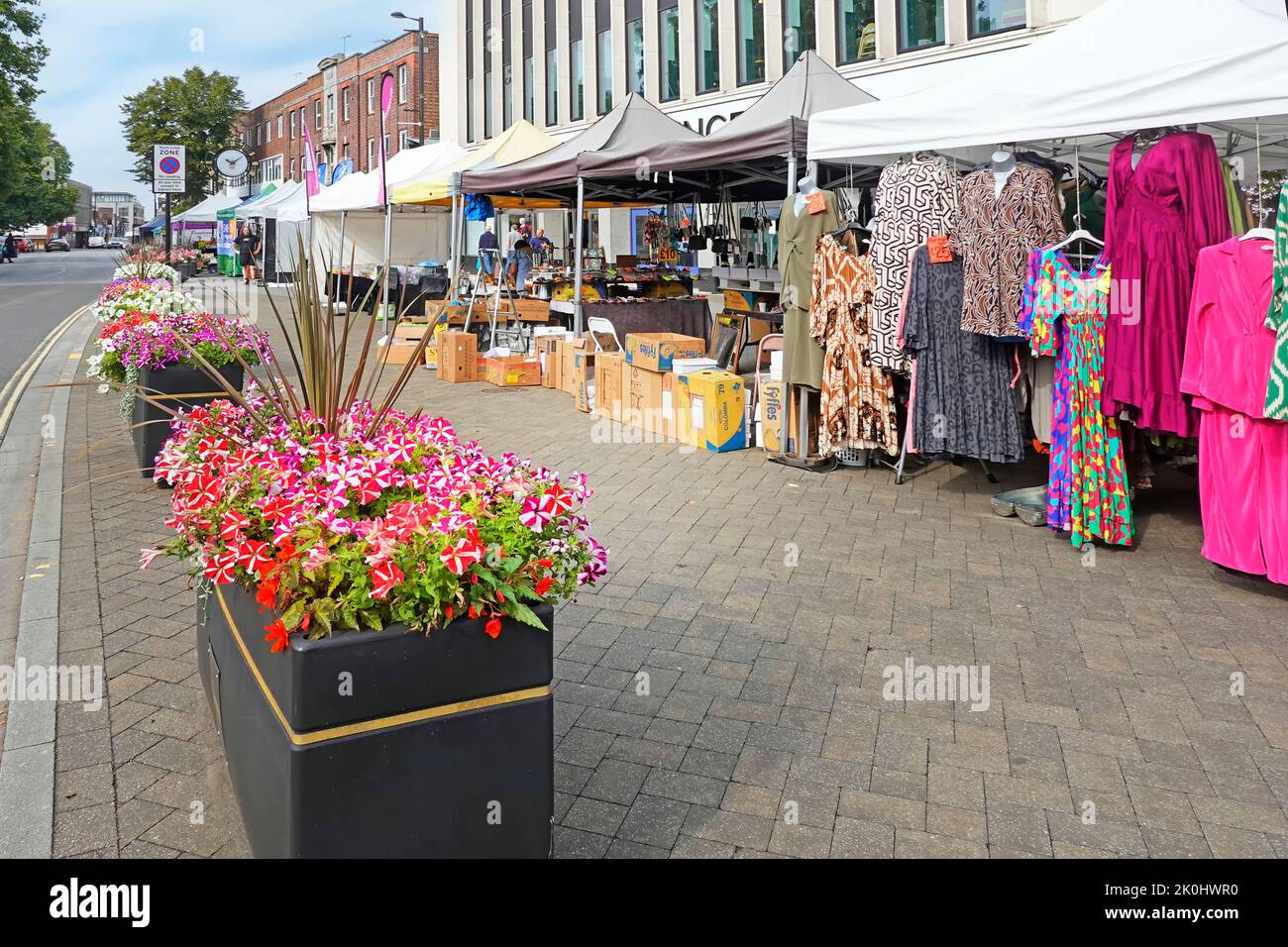 Colourful summer flowers in long row of rectangular planter boxes on market day clothing stall on wide pavement Brentwood High Street Essex England UK Stock Photo