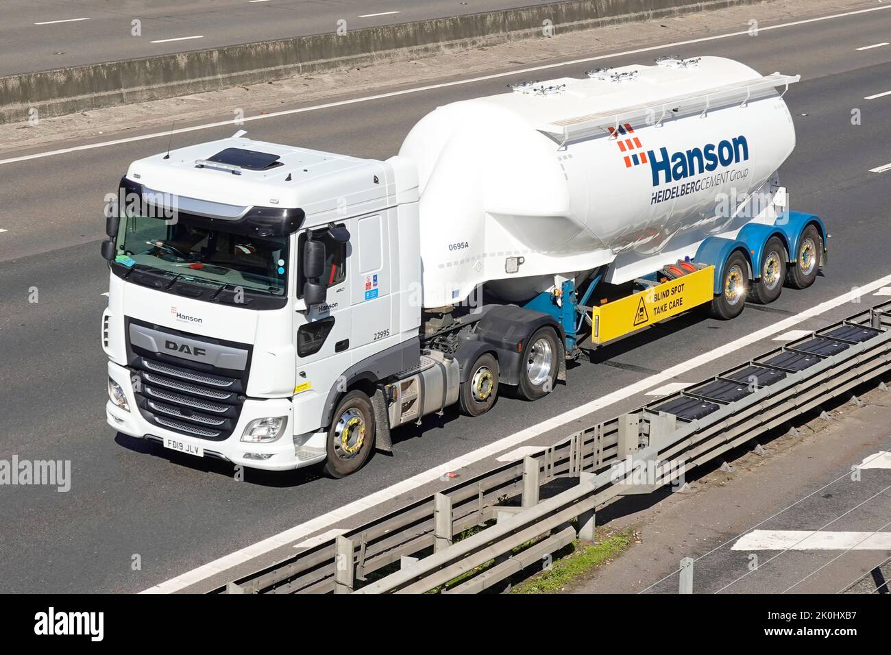 Logo & blind spot warning on side of Hanson Heidelberg bulk cement supply chain business group tanker trailer & hgv lorry truck driving on UK motorway Stock Photo