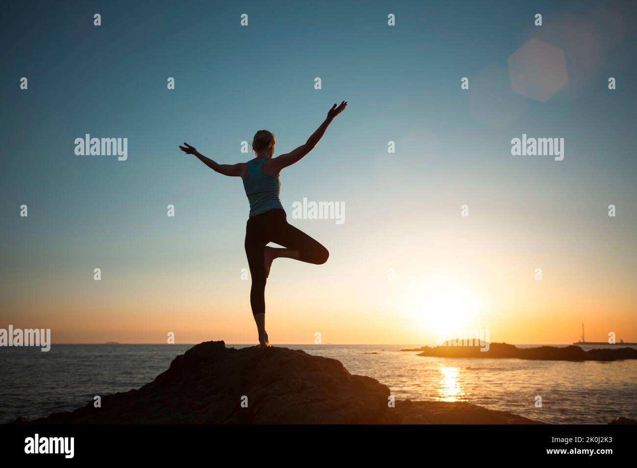 A woman does yoga, meditating near the ocean. A silhouette in the sunset. Stock Photo